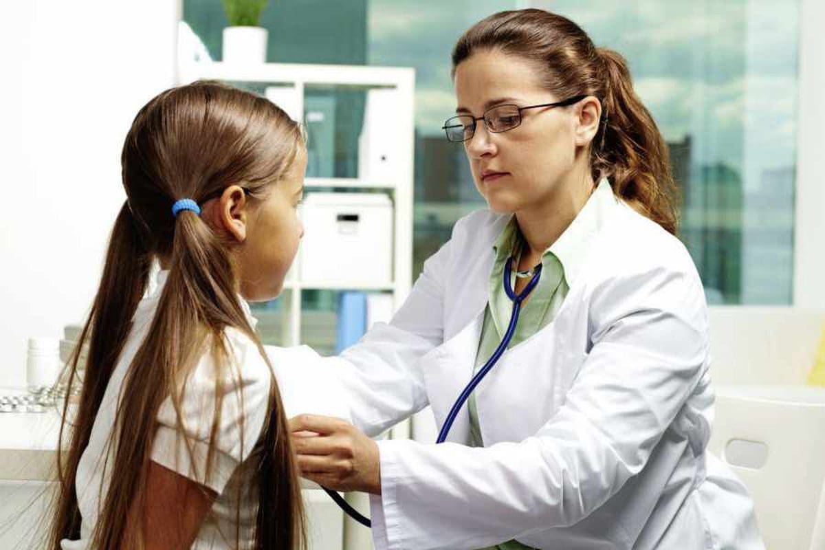 Female GP with glasses and stethoscope listens to girls chest